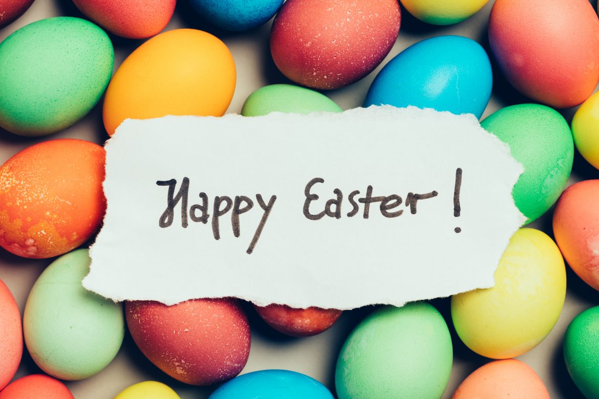 "Happy Easter" written on a piece of white paper. Colorful eggs. Holiday wishes.