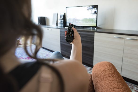 Woman hold TV remote control. TV on the background.