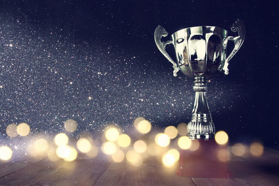 low key image of trophy over wooden table and dark background, with abstract shiny lights